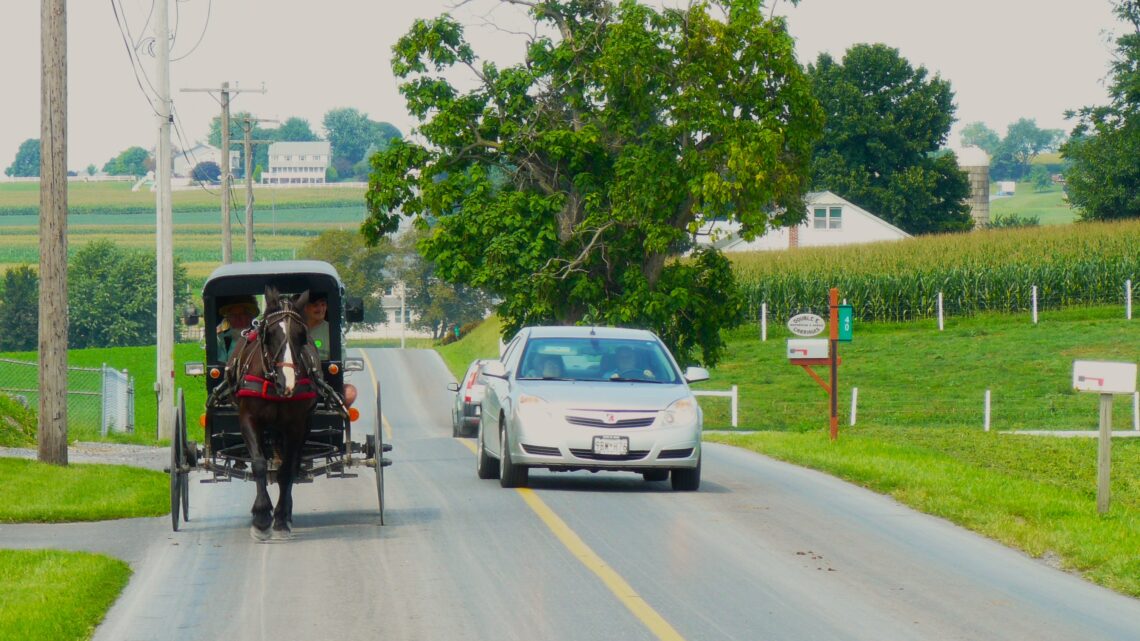A horse-drawn carriage with a modern car alongside it.