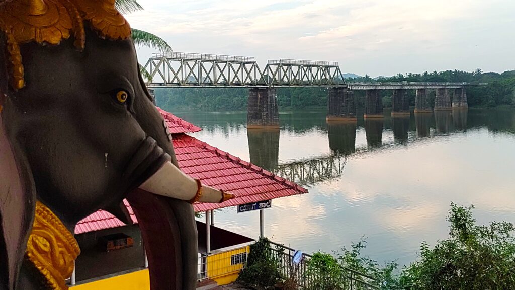 A close-up of an elephant statue, with the railway bridge across the Netravati Bridge.